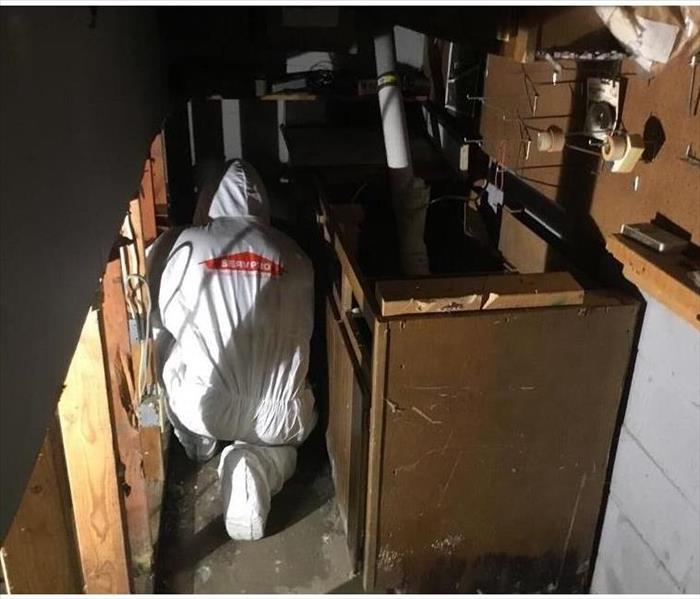 Technician in white biohazard coveralls removing cabinets in basement