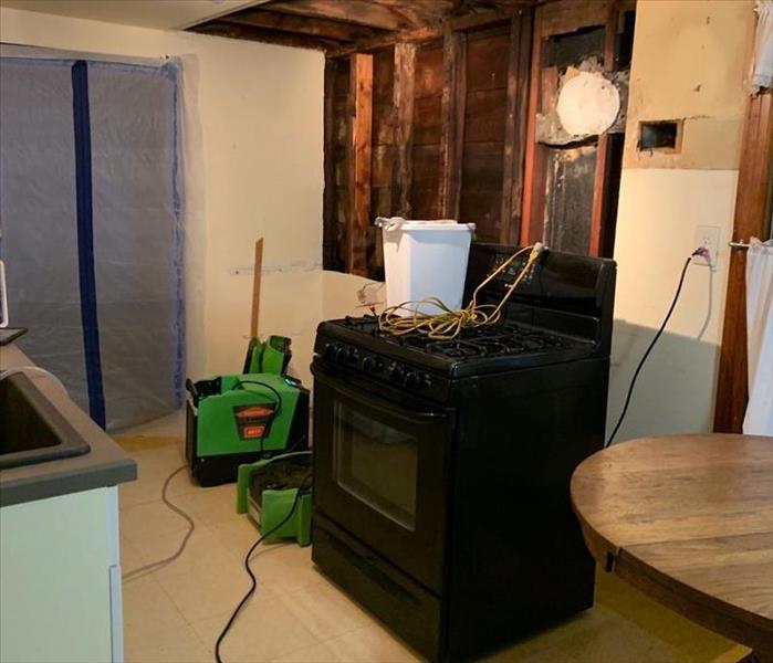 A photo of a kitchen with walls removed, plastic containment on the doorway and green SERVPRO equipment set up for drying