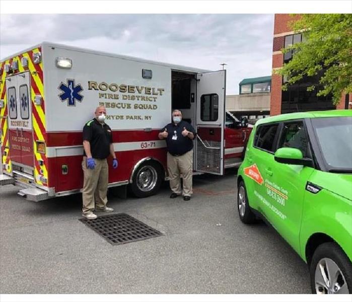 2 people posing for a photo in front of an ambulance and a green SERVPRO vehicle.