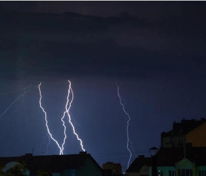 A photo of several white lightning strikes hitting homes and businesses against a dark blue sky.