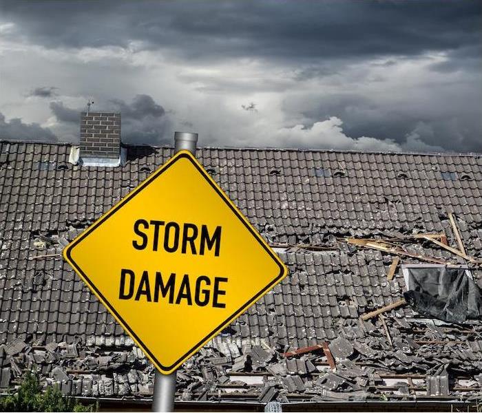 A yellow storm damage sign posted in front of a heavily damaged roof of a home.