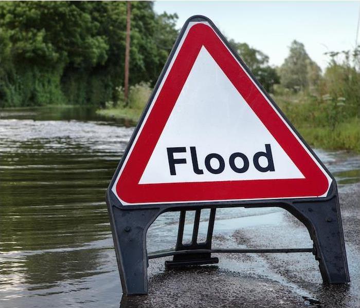 A red and white triangle sign with the word "Flood" on it placed on a flooded out roadway.