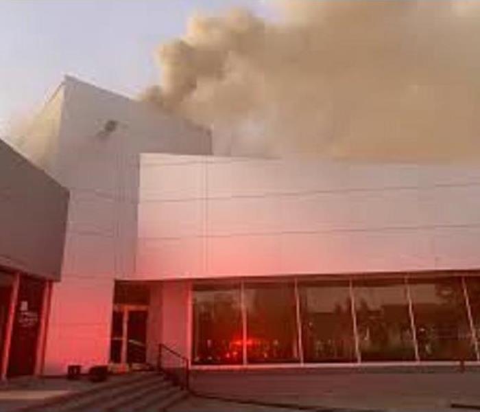 A commercial office building with plumes of smoke coming up from the back.