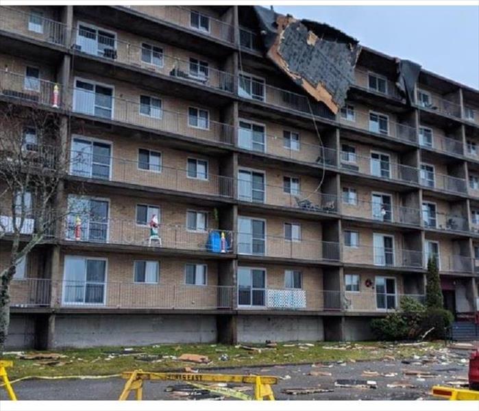 A multi-level apartment building with structural roof and siding damage after a storm.