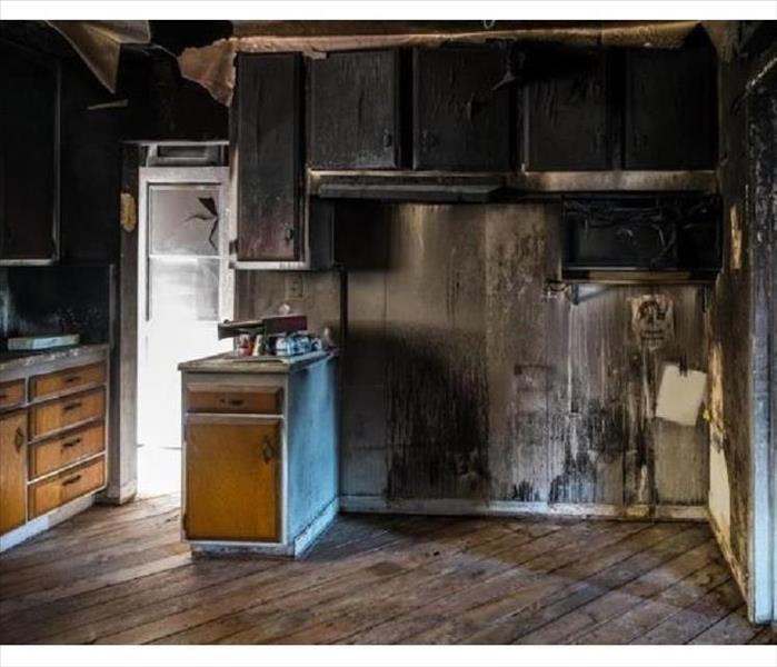 A photo of a burned kitchen in a home, cabinets blackened and appliances removed.