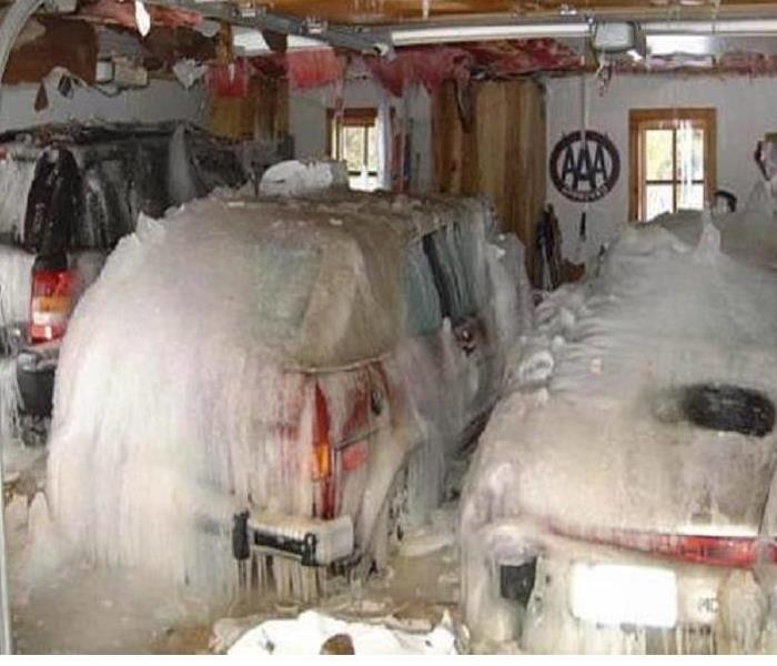 A photo of a home garage with 3 cars completely encased in ice from a burst pipe in the ceiling above.