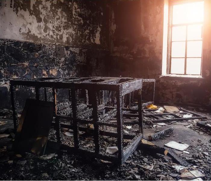A heavily burned room with scorched walls, a charred desk, dresser and bed frame
