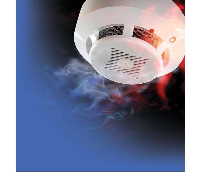 A white smoke detector on a blue and red background with smoke trails close to it