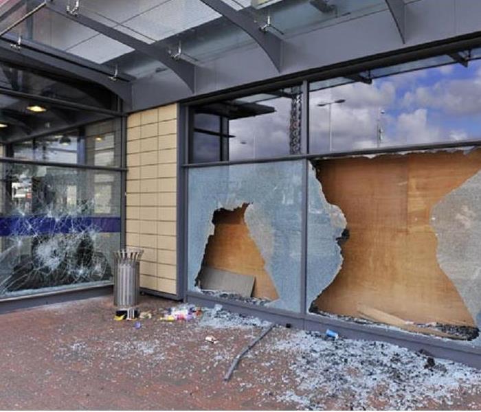 A storefront with glass broken out and entrance boarded up